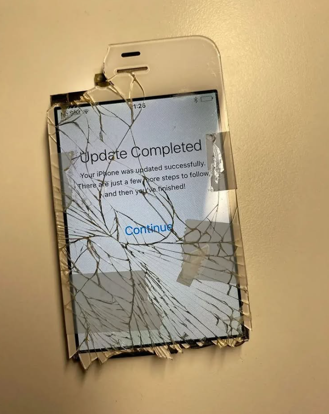 a broken iphone 4/s with shattered glass, no bottom, and a chipped top. the screen reads "Update Completed"